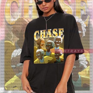 May include: Black unisex t-shirt featuring a graphic of a group of elderly men with the word "CHASE" in gold lettering. The shirt is a comfortable oversized fit.