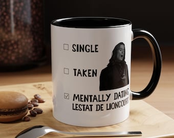 Puede incluir: Una taza de cerámica blanca con interior y asa negros. El exterior presenta una lista de verificación con el texto Single, Taken y Mentally Dating Lestat de Lioncourt, una marca de verificación junto a la última opción y un retrato de un hombre.