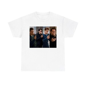 May include: A white short-sleeve t-shirt featuring a rectangular graphic print on the chest. The graphic displays four separate images of different individuals, each holding a smartphone and covering their mouth with their hand in a similar pose.