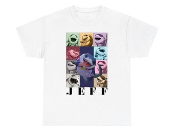 May include: A white t-shirt featuring a central graphic of a cartoon shark character named Jeff. The design includes a grid of smaller shark illustrations in various colors surrounding a larger central shark image, with the text JEFF below.