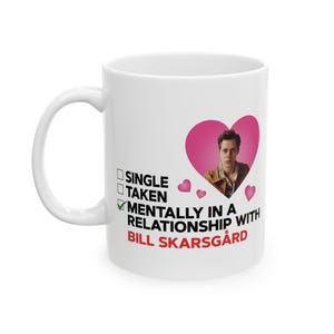 May include: White ceramic mug with a handle. The mug features a pink heart with a photo of a man inside. Text on the mug reads "Single", "Taken", and "Mentally in a relationship with Bill Skarsgård".