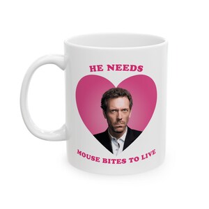 May include: White ceramic mug with a pink heart featuring a photo of a man with the text "HE NEEDS MOUSE BITES TO LIVE" printed on it.