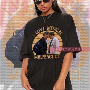 Puede incluir: Una camiseta negra con un gráfico de estilo vintage de dos hombres en un entorno médico. El gráfico incluye el texto "Me encanta la mala praxis médica".