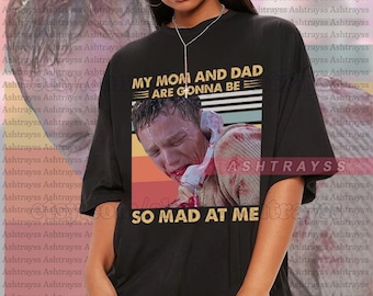 Może przedstawiać: Czarny t-shirt unisex z napisem "MY MOM AND DAD ARE GONNA BE SO MAD AT ME" i grafiką mężczyzny przy telefonie. Koszulka jest w rozmiarze oversize i wykonana z miękkiego materiału.