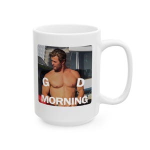 Könnte beinhalten: Ein weißer Keramikbecher mit einem rechteckigen Fotodruck einer oberkörperfreien Person mit kurzem braunem Haar, die zur Seite blickt. Der weiße Text G D MORNING ist über das Bild gelegt, wobei die Buchstaben G und D den Oberkörper flankieren.