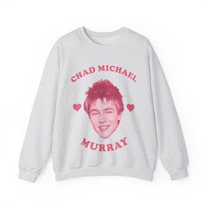 May include: A gray sweatshirt with a pink graphic of a man's face with the text "Chad Michael Murray" in a pink circle around the face and two pink hearts on either side of the face.