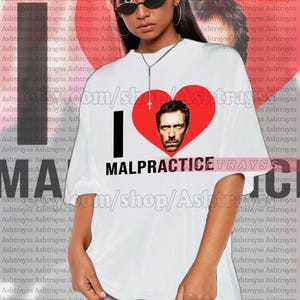 Puede incluir: Camiseta blanca con un corazón rojo que presenta un retrato de un hombre. El texto "I ♥ MALPRACTICE" está impreso en la camiseta. La modelo lleva una camiseta talla 2XL. Es una camiseta unisex de talla real, y para conseguir el look de talla grande, tienes que elegir +1 o +2 de tu talla original.