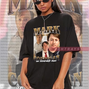 Peut inclure: T-shirt noir unisexe avec un graphisme de trois hommes et le mot "MARK" en or. La phrase "Corrigan an honorable man" est en dessous. Le modèle porte une taille 2XL. Le t-shirt est ample.