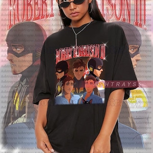 May include: Black unisex t-shirt with a graphic of animated characters and the text "ROBERT ROBERTSON III". The shirt has an oversized fit and is made of a soft fabric.