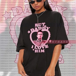 May include: Black unisex t-shirt with the text "BUT DADDY I LOVE HIM" in pink, featuring a heart-shaped design with a portrait. The shirt is oversized and suitable for various body types.