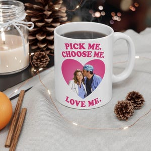 May include: A white ceramic mug featuring a pink heart graphic containing a photograph of two people in medical scrubs. Above the heart, the text reads PICK ME. CHOOSE ME. and below the heart, the text reads LOVE ME. in bold pink lettering.