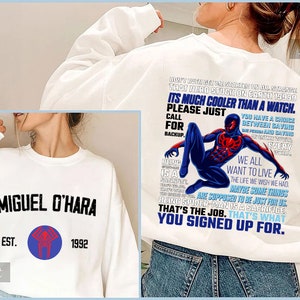 Könnte beinhalten: Weißes Sweatshirt mit der Aufschrift "MIGUEL O'HARA EST. 1992" auf der Vorderseite. Auf der Rückseite befindet sich eine Grafik eines Superhelden und Text, darunter "IT'S MUCH COOLER THAN A WATCH" und "THAT'S WHAT YOU SIGNED UP FOR."