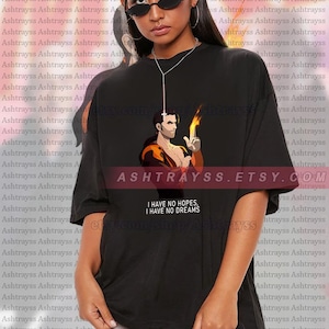 May include: Black unisex t-shirt featuring a graphic of a man holding a flame, with the text "I HAVE NO HOPES, I HAVE NO DREAMS" and the shop's Etsy URL. The model is wearing a 2XL shirt.