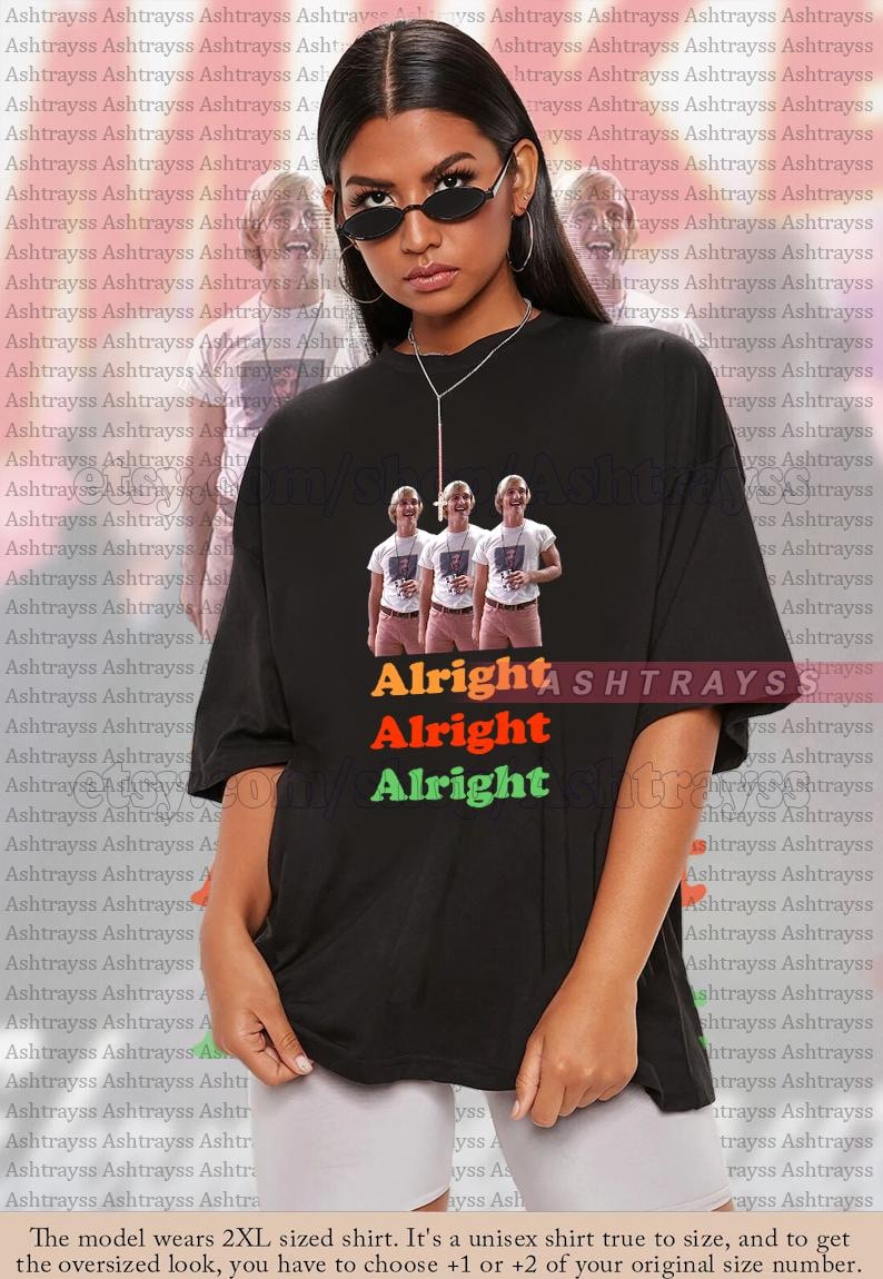 May include: Black unisex t-shirt featuring a graphic of three people with the text "Alright Alright Alright" in orange, red, and green. The shirt is oversized and has a crew neck.