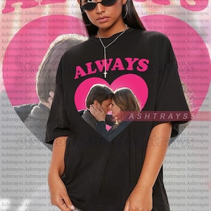 May include: Black unisex t-shirt featuring the word "ALWAYS" in pink, a pink heart design, and a photo of a kissing couple. The shirt is oversized and made of a soft fabric.