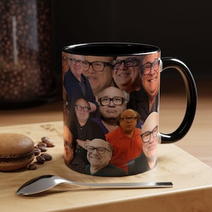 Può includere: Una tazza in ceramica con interno e manico neri, caratterizzata da un collage di molteplici ritratti fotografici dell'attore Danny DeVito con occhiali dalla montatura nera. La tazza mostra varie espressioni facciali e pose.