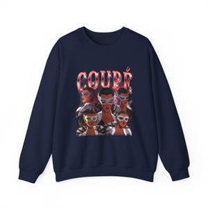 May include: A navy blue sweatshirt with a graphic of masked figures and the word "COUPÉ" in red. The design features multiple faces with masks. The sweatshirt has a crew neck and long sleeves.