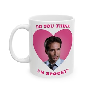 Puede incluir: Taza de cerámica blanca con un diseño de corazón rosa. La taza presenta un retrato de un hombre y el texto "DO YOU THINK I'M SPOOKY?" en letras rosas. La taza tiene un asa blanca.