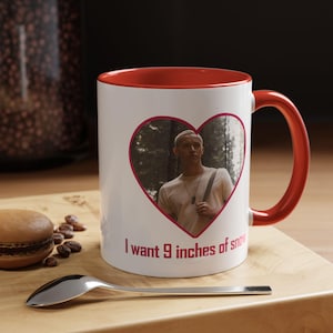 Könnte beinhalten: Ein weißer Keramikbecher mit rotem Innenraum und rotem Henkel. Auf der Vorderseite befindet sich ein herzförmiger Rahmen mit einem Foto einer Person im Wald und dem roten Text "I want 9 inches of snow" unter dem Herzmotiv.