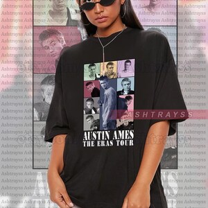 May include: Black unisex t-shirt with a collage of images and the text "AUSTIN AMES THE ERAS TOUR". The shirt is oversized and has a crew neck.