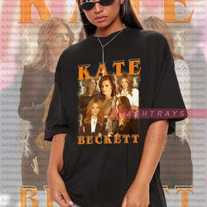 Puede incluir: Camiseta unisex negra con la palabra "KATE" en naranja y un collage de fotos de mujeres. La palabra "BECKETT" está debajo. La modelo lleva una talla 2XL. La camiseta es fiel a la talla.