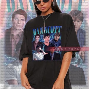 Puede incluir: Camiseta negra con un estampado gráfico de una banda llamada "Dan Scott". El gráfico presenta a cinco hombres en un estilo collage con rayos en el fondo.