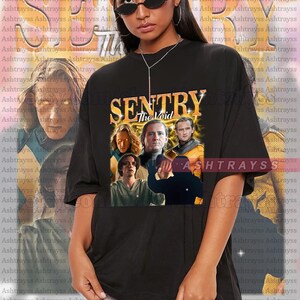 May include: Black oversized t-shirt with a graphic print of a group of people with the text "SENTRY The Void" in yellow and orange. The shirt is a unisex style and is available in multiple sizes.
