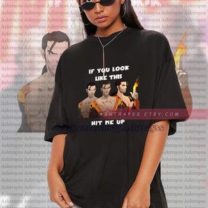 May include: Black unisex t-shirt featuring a graphic with three stylized figures and the text "IF YOU LOOK LIKE THIS HIT ME UP" in white. The Etsy shop URL is also visible. The model is wearing the shirt.