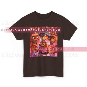 Puede incluir: Una camiseta marr&oacute;n oscuro con un gr&aacute;fico del personaje Nick Wilde de la pel&iacute;cula animada Zootr&oacute;polis. El gr&aacute;fico incluye m&uacute;ltiples im&aacute;genes de Nick Wilde y el texto "NICK WILDE". La URL de la tienda Etsy es visible.
