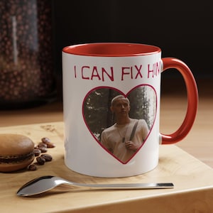 Peut inclure: Un mug en céramique blanche avec un intérieur et une anse rouge vif. L'avant présente le texte I CAN FIX HIM en lettres rouges au-dessus d'un cadre en forme de cœur contenant le portrait photographique d'une personne portant un haut clair.