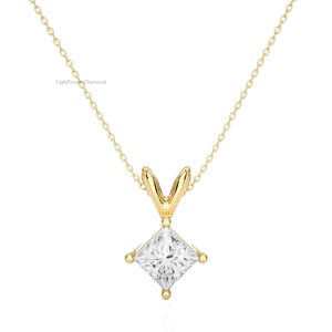 May include: A gold-colored necklace with a square, clear gemstone pendant. The pendant is held by a four-prong setting. The necklace chain is delicate and gold-colored. The jewelry is displayed against a white background.