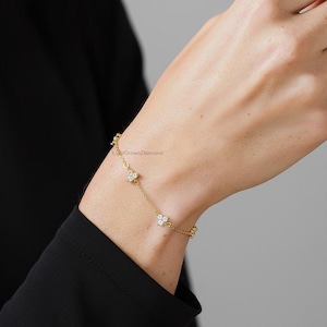 Puede incluir: Una delicada pulsera dorada con tres colgantes en forma de flor con piedras preciosas transparentes. La pulsera se lleva en la muñeca, mostrando sus finos detalles y su elegante diseño. Una hermosa pieza de joyería.