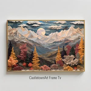 May include: A framed paper art print depicting a mountain range with a full moon in the sky. The mountains are layered with different shades of blue, brown, and white. The foreground features a forest of trees with autumn foliage in shades of red, orange, and yellow.