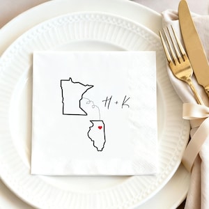 May include: White square napkin with a black outline of two states, Minnesota and Illinois, connected by a dotted line. A red heart is in Illinois. The initials "H + K" are written in black script.