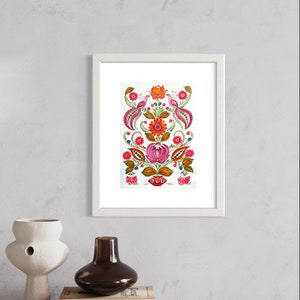 Può includere: Una stampa floreale incorniciata con un bordo bianco. L'opera presenta un design simmetrico di fiori e uccelli rossi, rosa, arancioni e verdi. La stampa è esposta su una superficie di legno con vasi decorativi e libri.