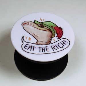May include: White phone grip with a cartoon illustration of a lizard wearing a green and red hat. The text "EAT THE RICH!" is written in a banner below the lizard.