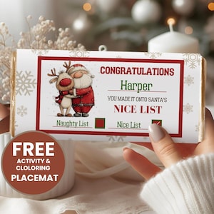 Puede incluir: Una barra de chocolate con temática navideña con una etiqueta roja y blanca. La etiqueta presenta una ilustración de Papá Noel y un reno, con el texto "CONGRATULATIONS Harper YOU MADE IT ONTO SANTA'S NICE LIST". También se incluye un mantel individual de actividades gratuito.