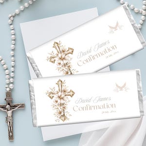 May include: Two white chocolate bar wrappers with a gold cross and floral design, and the text "David James Confirmation 28 July 20xx". A dove graphic is also present. The bars are on a light blue surface with a rosary and white flowers.