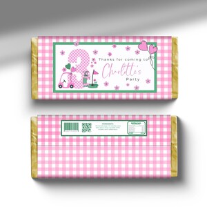 以下が含まれることがあります： ピンクとグリーンのゴルフをテーマにしたチョコレートバーのラッパー。ピンクのゴルフカート、ゴルフクラブ、数字の3が描かれています。ラッパーには「Charlotte's Partyへようこそ」という文字が書かれています。