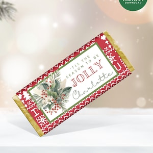 Könnte beinhalten: Eine weihnachtliche Schokoriegelverpackung mit einem rot-weißen Schneeflockenmuster. Die Verpackung zeigt den Text "'TIS THE SEASON TO BE JOLLY Charlotte" und ein Blumendesign mit Beeren und Grünzeug. Ein grüner Kreis mit "INSTANT DOWNLOAD" befindet sich oben rechts.