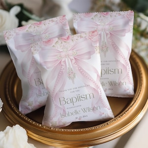 Puede incluir: Tres bolsas rectangulares para recuerdos con un diseño floral en rosa y blanco, un gran lazo rosa central y un gráfico de una cruz. El texto dice: Thank you for joining us for the Baptism of our daughter Isabelle Wilson 10-23-20xx.