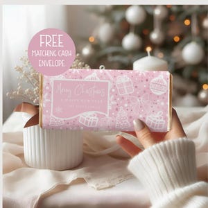 Könnte beinhalten: Rosa Geschenkpapier mit weihnachtlichen Motiven, darunter Geschenke, Ornamente und Schneeflocken in Weiß. Der Text lautet "Merry Christmas & A Happy New Year, The Scott Family." Ein passender Umschlag ist enthalten.