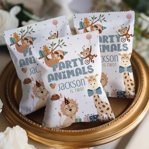 May include: Three white party favor bags with the text "PARTY ANIMALS JACKSON IS TWO!" and illustrations of a sloth, monkey, lion, and giraffe. The bags are decorated with balloons, gifts, and confetti, perfect for a child's birthday party.