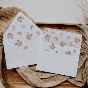 May include: A white envelope with a floral pattern on the front and a smaller white envelope inside. The floral pattern features pink and white roses.