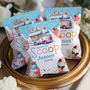 Könnte beinhalten: Drei Party-Geschenktüten mit Eiscreme-Motiv. Jede Tüte zeigt eine Eiswagen-Illustration, Eistüten und den Text "Here's the Scoop James is Four". Die Tüten befinden sich auf einem goldfarbenen Tablett.
