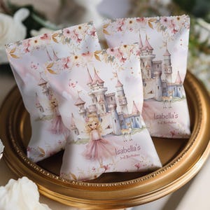 May include: Three party favor bags with a fairytale castle design. The bags feature a pink and white colour scheme with illustrations of a castle, a girl in a pink dress, and deer. The text "Isabella's 3rd Birthday" is printed on the bags.