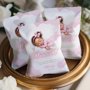 May include: Three pink and white baby shower favor bags with a sleeping baby illustration. The bags feature text that reads "A little piece of Heaven" and "Olivia". The bags are on a gold-colored tray.