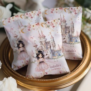 Puede incluir: Tres bolsas de fiesta con temática de princesa. Cada bolsa presenta una ilustración de castillo, una niña con un vestido rosa y el texto "Isabella's 3rd Birthday". Las bolsas están decoradas con detalles florales y mariposas.
