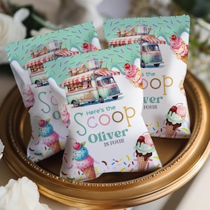 May include: Three party favor bags with an ice cream theme. Each bag features an ice cream truck illustration, ice cream cones, and the text "Here's the Scoop Oliver is Four". The bags are on a gold-colored tray.