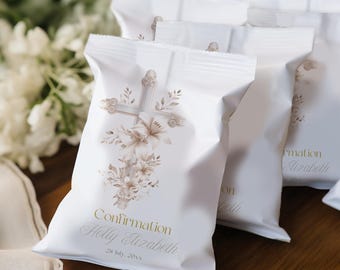 Könnte beinhalten: Weiße Gastgeschenktüten mit Kreuz- und Blumendesign. Die Tüten tragen das Wort "Confirmation" sowie einen Namen und ein Datum in Gold. Die Tüten sind versiegelt und liegen auf einer Holzoberfläche.